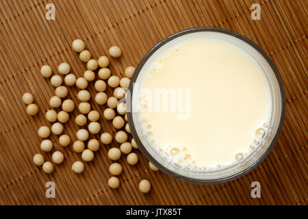 Glas Sojamilch mit Schaum auf Bambus Matte von oben. Verschüttete Sojabohnen. Stockfoto