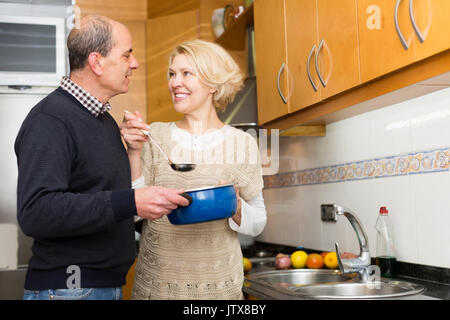 Glücklich lächelnde ältere Ehepartner Vorbereitung Essen in der modernen Küche. Fokus auf Frau Stockfoto