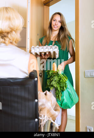 Alte Frau im Rollstuhl Konferenz Assistant mit Eiern vor der Haustür Stockfoto