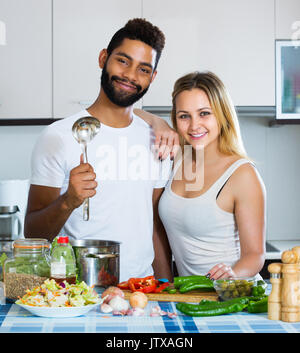 Junge interracial Paare Kochen Gemüse und lachend in der Küche Stockfoto