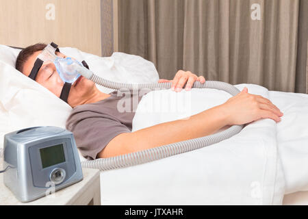 Mittelalter asiatischer Mann schläft in seinem Bett mit CPAP Maske verbinden mit Luftschlauch und CPAP-Gerät, Gerät für Menschen mit Schlafapnoe Stockfoto