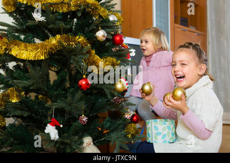 Zwei freundlich lächelnden kleinen Schwestern schmücken Weihnachtsbaum zu Hause Stockfoto