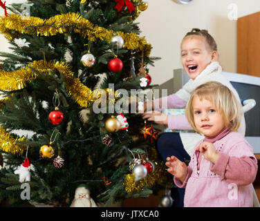 Zwei fröhliche kleine Schwestern schmücken Weihnachtsbaum zu Hause Stockfoto