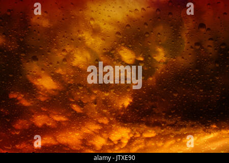 Blick durch eine misty Fenster mit Regentropfen auf die dramatischen Sturm Wolken bei Sonnenuntergang brauen Stockfoto