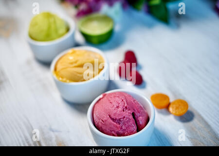 Auswahl an Gourmet Aromen der italienischen Eis in lebendigen Farben in einzelnen Porzellan Tassen auf einem alten rustikalen Holztisch serviert in einer Eisdiele, Betrachtungswinkel und jpg Stockfoto