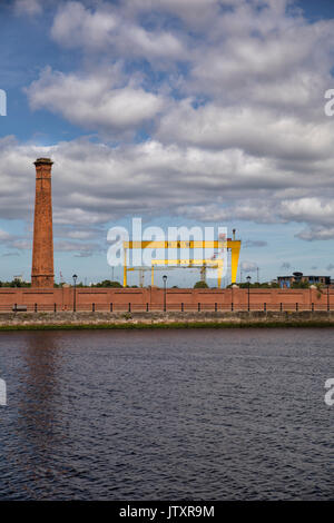 Belfast, ein Blick auf die alte Werft Harland und Wolff Krane (Samson und Goliath) mit Fluss Lagan, Schornstein und Red brick wall im Vordergrund Stockfoto