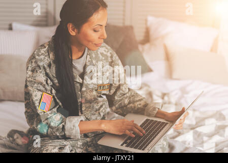 Militärische Frau plaudern auf dem Laptop im Bett Stockfoto