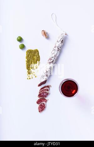 Fuet - Salami mit Rotwein. Fleisch Snack mit Oliven, Knoblauch und Pesto. Weißer Hintergrund, Ansicht von oben. Stockfoto