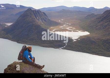 Ein Wanderer ist, genießen die Aussicht über Fjord und Berge, während auf einem Felsen des berühmten besseggen Grat in Norwegen sitzen. Diese 1 Tag fahren in Jotunheimen Nationalpark ist die beliebteste Wanderung in Norwegen. Stockfoto