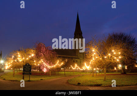 Weihnachtsbeleuchtungen verzaubern das Dorf unten grün St Peter's Church in Edensor, einem hübschen Dorf in der Peak District, Derbyshire, England, Großbritannien Stockfoto