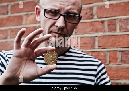 Jungen weißen Mann mit litecoin Münze in der Hand. Outdoor brickwall Konzept. Stockfoto