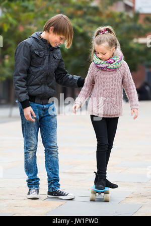 Happy Teenager Lehre jüngere Schwester skateboarding im Herbst Tag Stockfoto