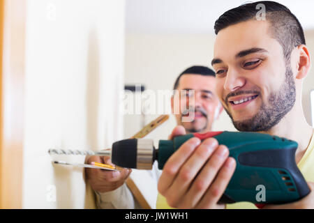 Junge positive Sohn und Vater bohren an der Wand im Innenbereich Stockfoto