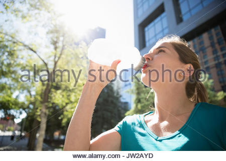 Läuferin Trinkwasser aus der Flasche Wasser im sonnigen städtischen Park