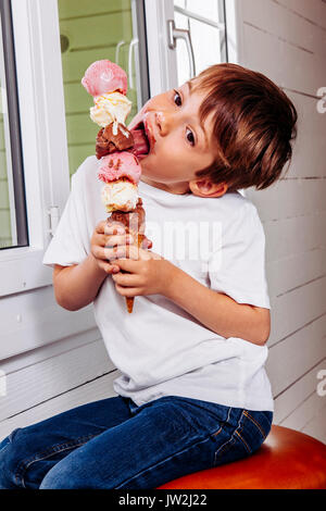 Foto von einem 6 Jahre alten Essen ein großes Eis mit sechs Kugeln Schokolade, Vanille und Erdbeere. Stockfoto