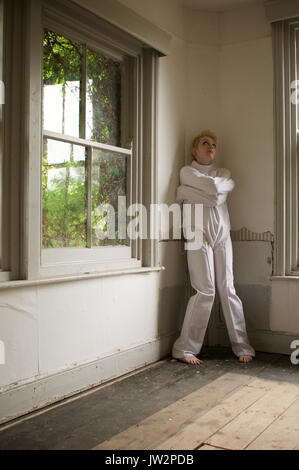 Mädchen in einer Zwangsjacke in einem verlassenen Haus Stockfoto