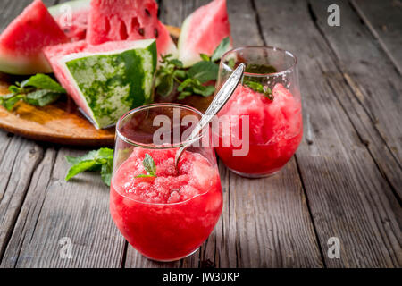 Sommer Obst Desserts, Frozen Cocktails. Eis Granit von Wassermelone mit Minze, portioniert in Gläsern, mit Scheiben von Wassermelone. Auf alten rustikalen w Stockfoto