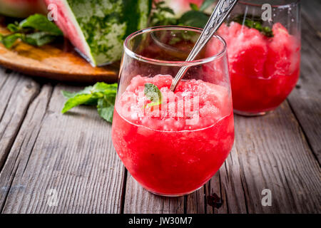 Sommer Obst Desserts, Frozen Cocktails. Eis Granit von Wassermelone mit Minze, portioniert in Gläsern, mit Scheiben von Wassermelone. Auf alten rustikalen w Stockfoto