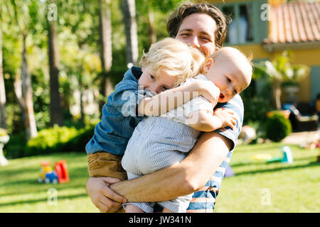 Vater mit zwei Söhnen (12-17 Monate, 4-5) beim Spielen im Hinterhof Stockfoto