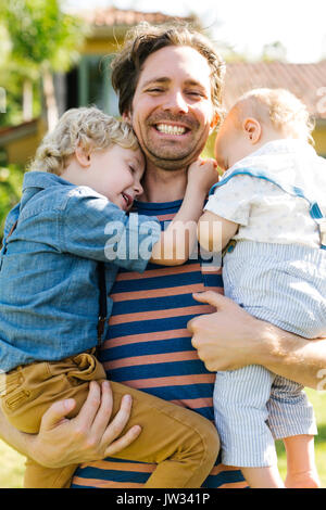 Vater mit zwei Söhnen (12-17 Monate, 4-5) beim Spielen im Hinterhof Stockfoto