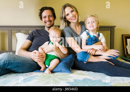 Portrait von Eltern mit Kinder (12-17 Monate, 4-5) auf Bett Stockfoto