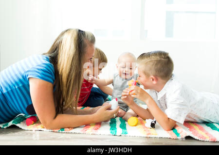 Mutter spielt mit ihren drei Kindern (6-11 Monate, 2-3, 6-7) Stockfoto