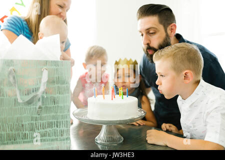 Familie mit vier Kindern (6-11 Monate, 2-3, 6-7) bläst die Kerzen auf der Geburtstagstorte Stockfoto