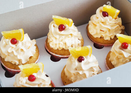 Vanille Cupcakes mit einer Kappe Luft der Creme mit Orange auf einem weißen Tisch mit Sahne in das Feld Stockfoto