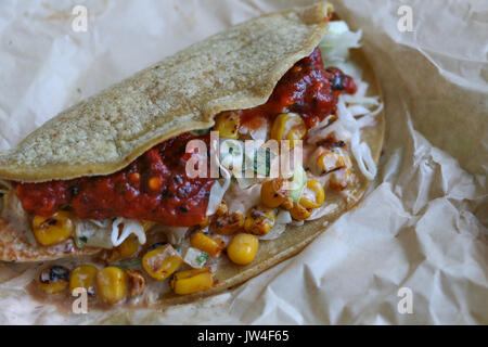 Nahaufnahme von einem bunten Fischen Taco, von Hand gefertigt mit Mais tortilla gefüllt mit Mais, Kohl, Salsa, und Koriander unter natürlichem Licht auf einem Papier Wrapper Stockfoto