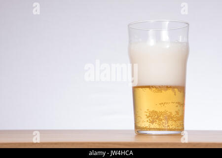 Eine eisige Kälte Glas, Hälfte mit Sekt Bier auf einem Holz Tisch mit weißem Hintergrund und kopieren Raum gefüllt. Stockfoto