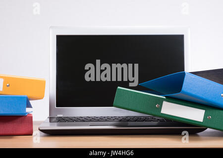 Ein unordentliches Büro Schreibtisch mit Computer, Laptop, Ordner und einem schlichten weißen Hintergrund mit kopieren. Stockfoto