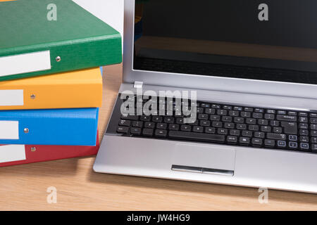 Ein ordentlich Holz Büro Schreibtisch Arbeitsbereich mit offenen Computer Laptop und ordentlich gestapelt Dokumentordnern. Stockfoto