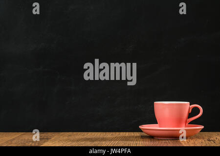 Rosa Kaffeetasse und die Platte ruhig auf hölzernen Boden auf blackboard Wand Hintergrund platziert und mit Raum für Werbung im Retro-stil Büro Studio. Stockfoto