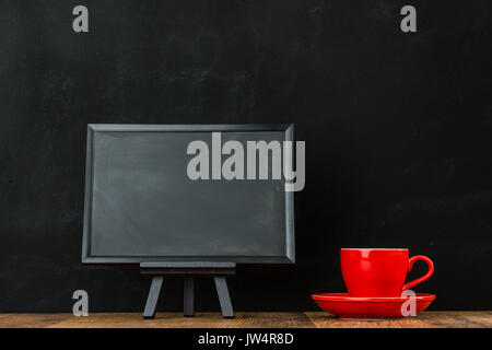 Foto zeigen kleine Tafel mit roten Kaffeetasse auf Holz Textur am Schreibtisch mit schwarzem Hintergrund Anzeige copyspace Kreide malen. Stockfoto