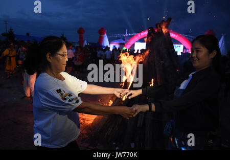 Xunke, Heilongjiang Provinz Chinas. 11 Aug, 2017. Die Menschen singen und tanzen um ein Lagerfeuer während des traditionellen Gott der ethnischen Gruppe der Brand Opfer Festival in Xunke County, im Nordosten der chinesischen Provinz Heilongjiang, Aug 11, 2017. Die Gulunmuta Festival, das wichtigste Festival für die oroqen Menschen, wurde als einer der ersten Charge von Chinas immaterielle Kulturerbe im Jahr 2006 aufgeführt. Credit: Wang Jianwei/Xinhua/Alamy leben Nachrichten Stockfoto