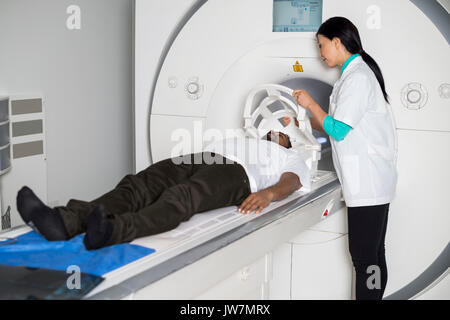 Ärztin zur Festsetzung Gesichtsmaske zu männlichen Patienten auf MRI-Scan im Krankenhaus liegenden Maschine Stockfoto