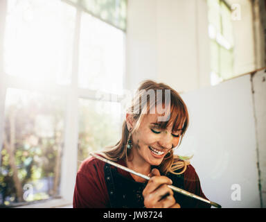 Innen- schuss der professionellen Künstlerin lächelnd mit Pinsel im Studio. Frau Maler Malerei in Ihrer Werkstatt. Stockfoto