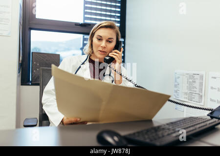 Arzt lesen medizinische Aufzeichnungen und Gespräche am Telefon. Medizin practitioner Prüfung ärztliche Berichte und verwenden Sie das Telefon in Ihrer Klinik. Stockfoto