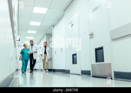 Volle Länge Schuß des medizinischen Teams gehen hinunter Flur im Krankenhaus. Ärzte mit Krankenschwester im Krankenhaus, Korridor und diskutiert. Stockfoto