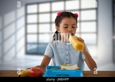 Mädchen trinken Saft bei Tisch gegen Zimmer mit großen Fenstern, Stadt Stockfoto