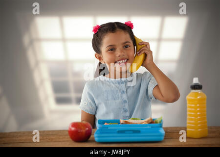 Lächelnde Mädchen mit Banane als Telefon gegen Zimmer mit großem Fenster, Stadt Stockfoto