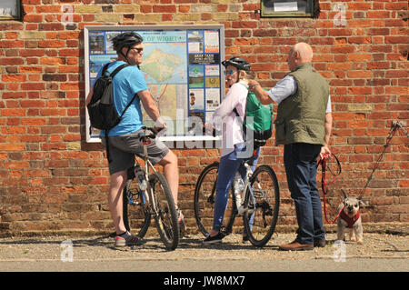 Eine Frau und ein Mann Frau Bitte Richtung für Radfahren als Radfahrer auf der Isle of Wight in Newport im Gespräch mit einem lokalen Mann mit Hund auf einer Karte suchen Stockfoto