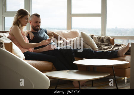 Romantisches Paar liegt auf dem Sofa und über Handy im Wohnzimmer Stockfoto
