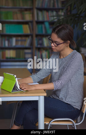 Weibliche Studentin mit digitalen Tablet während am Schreibtisch im Klassenzimmer studieren Stockfoto