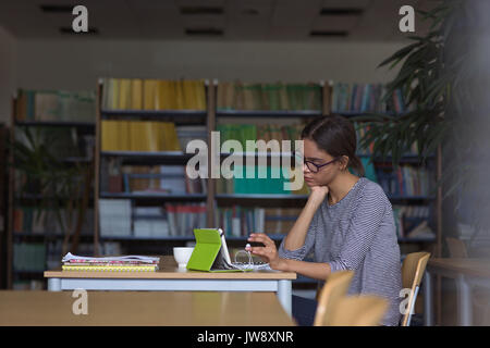 Weibliche Studentin mit digitalen Tablet während am Schreibtisch im Klassenzimmer sitzen Stockfoto