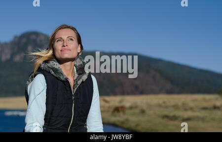 Lächelnde Frau weg schauen während der Sitzung gegen See während der sonnigen Tag Stockfoto