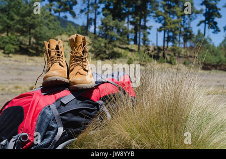 Nahaufnahme von Stiefel mit Rucksack auf dem Feld Stockfoto