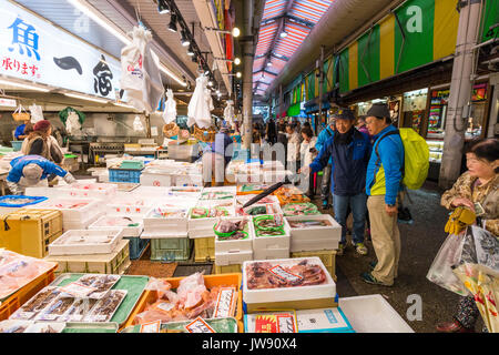 Einige Kunden auf der Suche nach frischen Seefisch in verschiedenen Box Container auf shop Front im Innen- Markt mit frischen Lebensmitteln festgelegt, Omicho, Kanazawa, Japan. Stockfoto