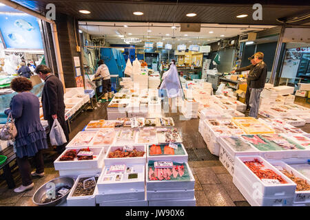 Einige Kunden auf der Suche nach frischen Seefisch in verschiedenen Box Container auf shop Front im Innen- Markt mit frischen Lebensmitteln festgelegt, Omicho, Kanazawa, Japan. Stockfoto