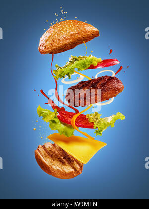 Die Hamburger mit fliegenden Zutaten auf blauem Hintergrund Stockfoto